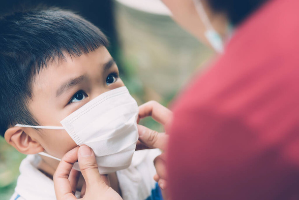 Μητέρα αναλάβει τη φροντίδα του γιου με μάσκα προσώπου για την προστασία της γρίπης της νόσου ή covid-19 σε εξωτερικούς χώρους, μαμά φορώντας ιατρική μάσκα με ασφάλεια των παιδιών για την προστασία ξέσπασμα πανδημίας στο κοινό, ιατρική έννοια. - Φωτογραφία, εικόνα