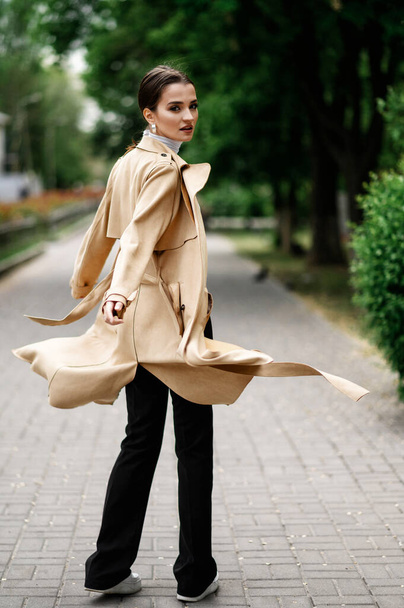 Beautiful brunette in a beige trench coat walking in the park - Fotoğraf, Görsel