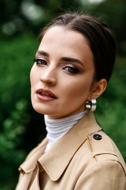 Beautiful brunette in a beige trench coat walking in the park - Photo, image