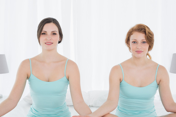 Portrait of two women sitting in meditation posture on bed - Zdjęcie, obraz