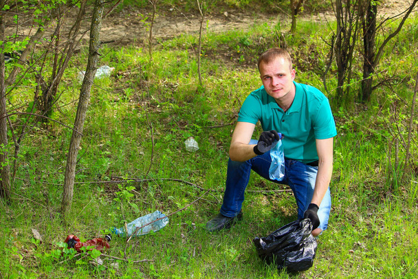 Vapaaehtoinen nuori mies Marrs vihreä t-paita roskapussi kerää muovi ei-hajoavia roskia luonnossa. - Valokuva, kuva