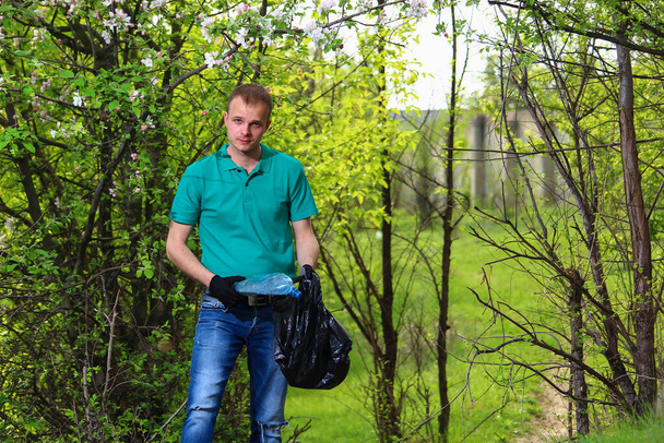 Vapaaehtoinen nuori mies Marrs vihreä t-paita roskapussi kerää muovi ei-hajoavia roskia luonnossa. - Valokuva, kuva