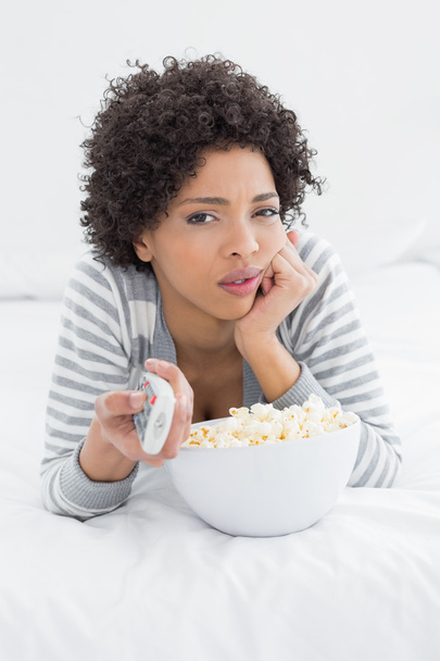 Woman with remote control and popcorn bowl lying in bed - Foto, afbeelding