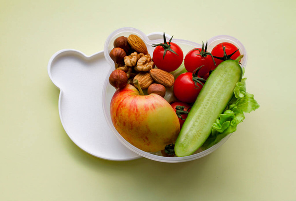 Kinder-Lunchbox in Form eines Bärenkopfes mit vegetarischer Kost: Gemüse, Obst, Nüsse. Mit Platz für Text, auf hellgelbem Hintergrund. Konzept der gesunden Ernährung, Snacks für Kinder - Foto, Bild