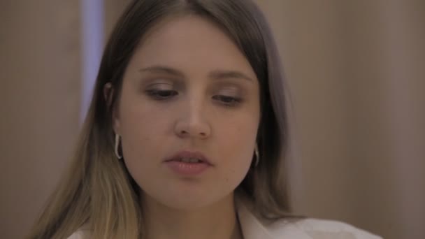 Girl actress of Slavic appearance in white shirt shows her emotions. Female is happy, picks up phone, talks and drinks coffee or tea. Close-up (face) of young woman - Metraje, vídeo