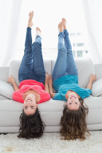 Smiling friends lying on sofa with legs in the air at home - Foto, Imagem