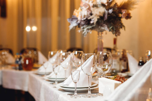 Nakrycie stołu weselnego pustymi kieliszkami. Bankiet selekcyjny z białymi serwetkami, talerzami i kieliszkami do wina białego i czerwonego na białym stole w restauracji - Zdjęcie, obraz