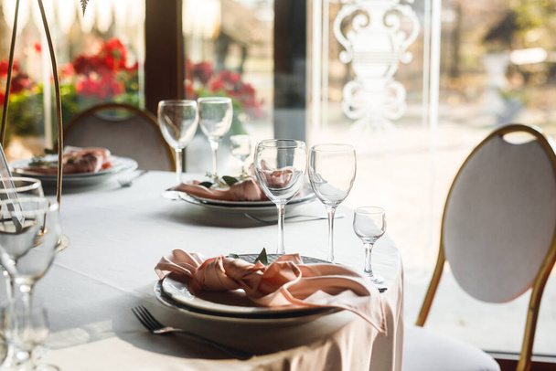 Ünnepi asztalterítők bezárása üres borospoharakkal és rózsaszín szalvétával. Ünnepi bankett fehér tányérokkal, rózsaszín szalvétával és borosüveggel fehér és vörösborhoz a fehér asztalon az étteremben - Fotó, kép