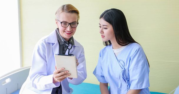 Lääkäri käyttää digitaalista tablettia selittääkseen lääkitystä naispotilaalle toimistossaan sairaaloissa
 - Valokuva, kuva