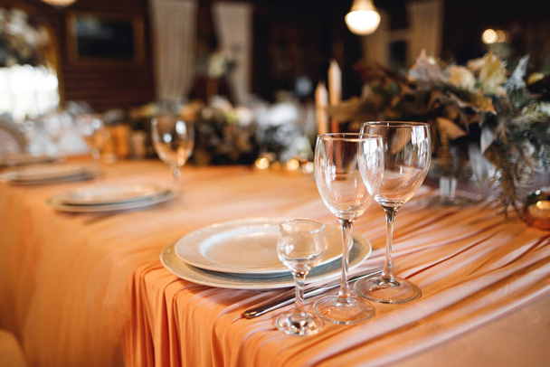 Festliche Tischdekoration mit leeren Weingläsern. Selebration Bankett mit weißen Servietten, Tellern und Weingläsern auf dem weißen Tisch im Restaurant. Drei Weingläser im Fokus - Foto, Bild