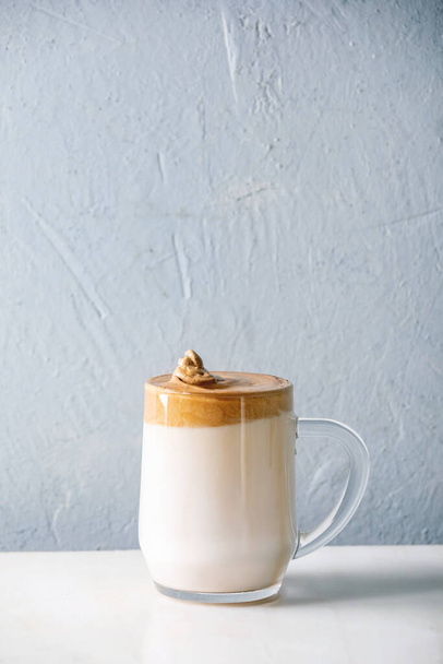 Dalgona frothy coffee trend korean drink milk latte with coffee foam in glass mug on white marble table. Copy space - 写真・画像