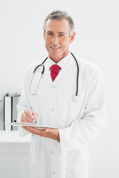 uśmiechnięty mężczyzna lekarz pisania raportu w urzędzie - Zdjęcie, obraz