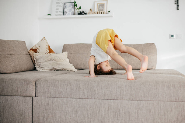 Cute little toddler girl tumbling on sofa at home. Child Learn To Tumble. Kids activity at home - Photo, image