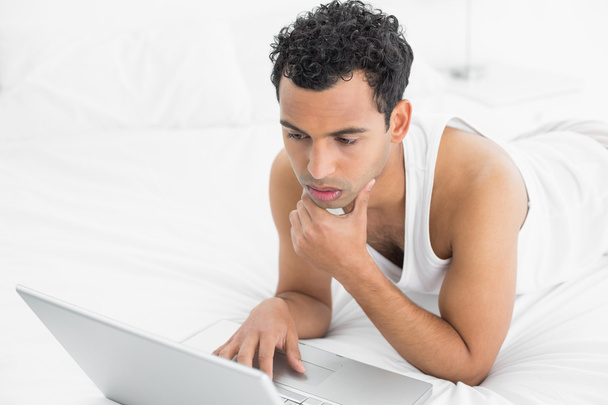 Casual young man using laptop in bed - Fotó, kép