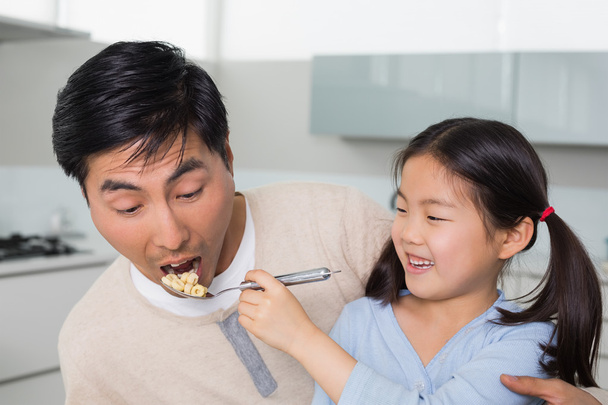 Young daughter feeding cereals to father in kitchen - Photo, image