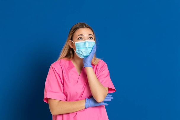 Joven médico con cara de máscara y uniforme rosa sobre fondo azul
 - Foto, imagen