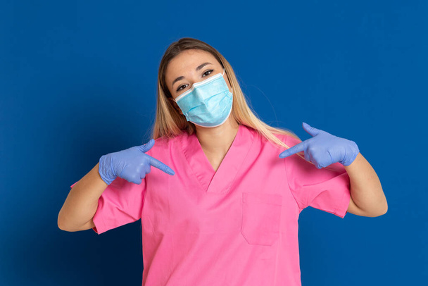 Young doctor wearing a mask face and a pink uniform on a blue background - Photo, image