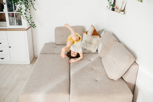 Cute little toddler girl tumbling on sofa at home. Child Learn To Tumble. Kids activity at home - Fotoğraf, Görsel