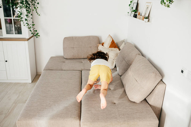 Beautiful little toddler tumbling on sofa at home. Child Learn To Tumble. Tumbling Tutorial. Gymnastics at Home, Tricks - 写真・画像