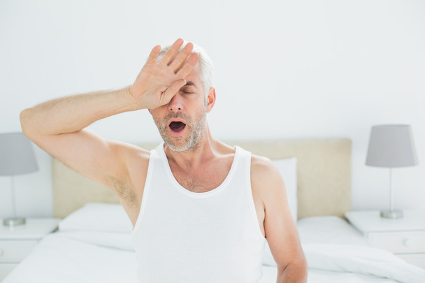 Mature man yawning in bed - 写真・画像