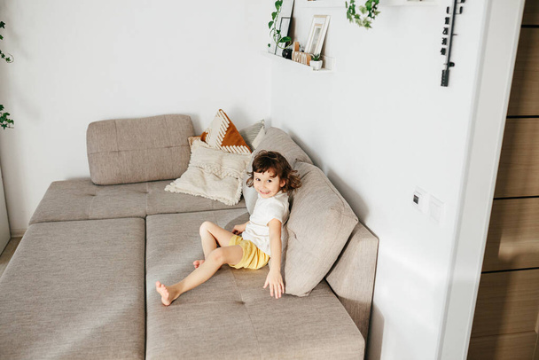 Счастливая и усталая симпатичная маленькая девочка на диване отдыхает после активной игры дома
. - Фото, изображение