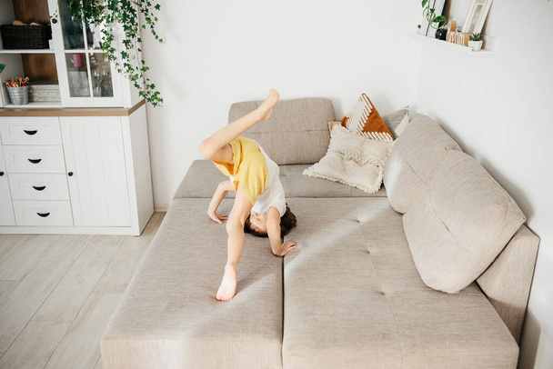Linda niña pequeña cayendo en el sofá en casa. El niño aprende a caer. Actividad infantil en casa
 - Foto, imagen