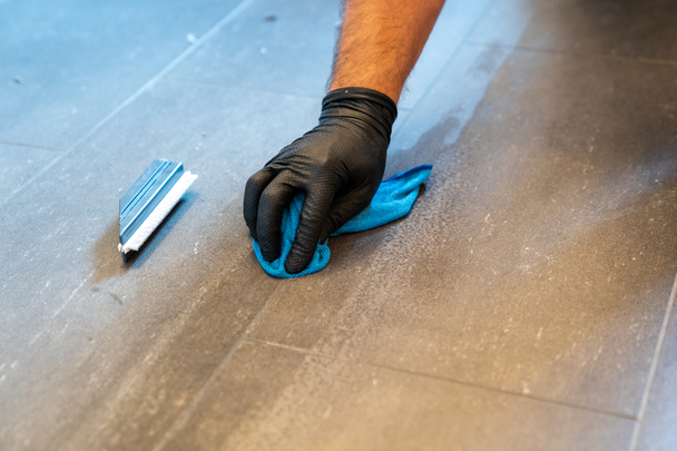 Eine Nahaufnahme einer professionellen Reinigungsfuge mit blauem Tuchtuch und schaumiger Seife auf einem grau gefliesten Badezimmerboden - Foto, Bild