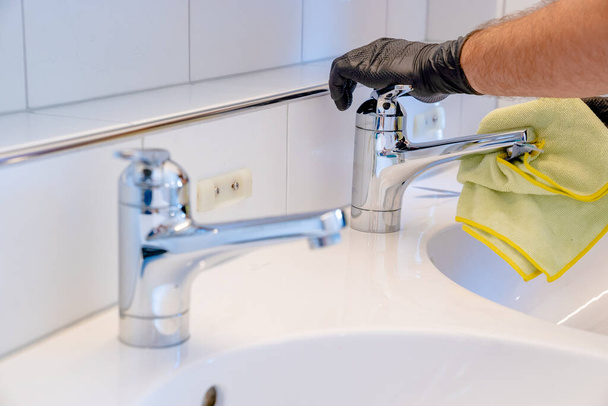 Un limpiador profesional pule un lavabo y un grifo del baño con un paño amarillo de la microfibra
 - Foto, Imagen