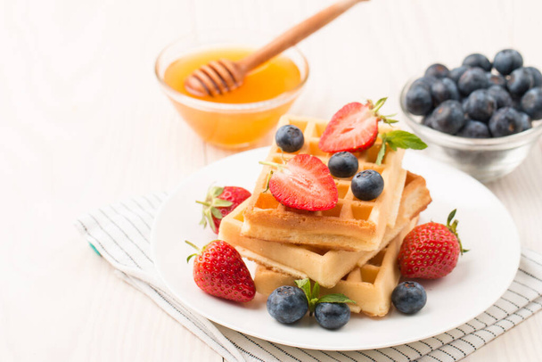 蜂蜜、チョコレート、イチゴ、ブルーベリーとベルギーのワッフルで作られた新鮮な自家製食品の写真。健康的なデザートの朝食コンセプト.  - 写真・画像