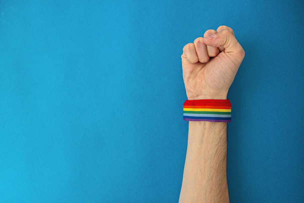 Punho mão com orgulho gay arco-íris bandeira pulseira em um fundo azul
 - Foto, Imagem