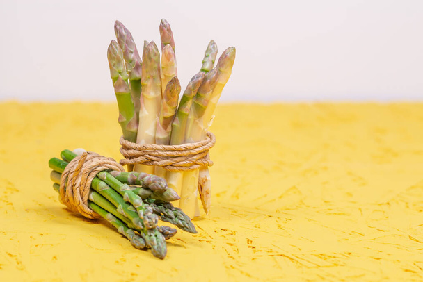 Green and white fresh asparagus tied with a yellow rope on a gray background. High quality photo - Foto, imagen
