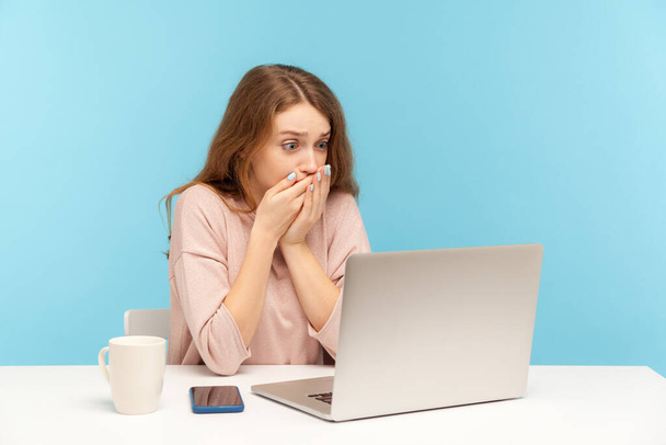 I won't tell anyone! Frightened woman employee covering mouth while communicating on video call, looking at laptop screen with terrified expression, found scary secret on internet. indoor studio shot - 写真・画像