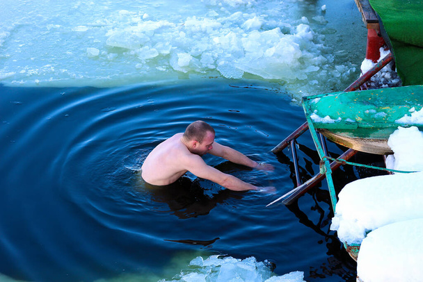Молодой человек спускается в ледяную дыру. Русское зимнее плавание. Холодное закаливание тела
. - Фото, изображение