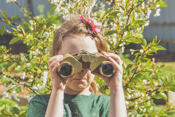 the child girl looking through binoculars on a background of flowers - Valokuva, kuva