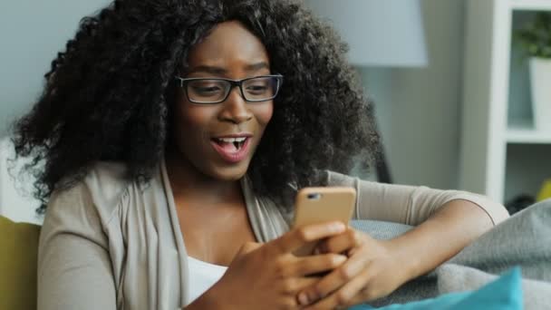 Young happy smiled African American woman chatting and laughing on her smart phone. Indoor. - Materiał filmowy, wideo