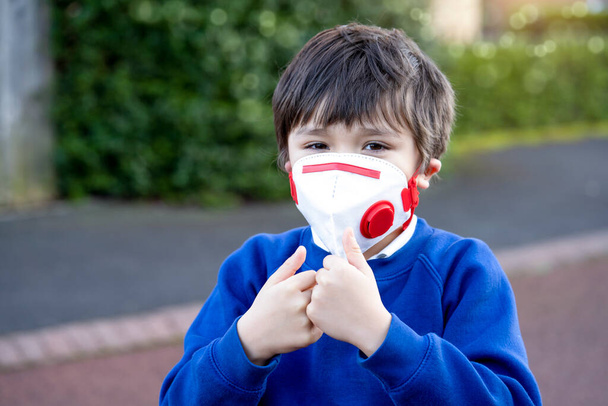Веселіше, коли дитина носить захисну маску для забруднення або вірусу, дитина у шкільній формі носить медичну маску і показує пальці, готові повернутися до школи після того, як Ковід блокує. - Фото, зображення