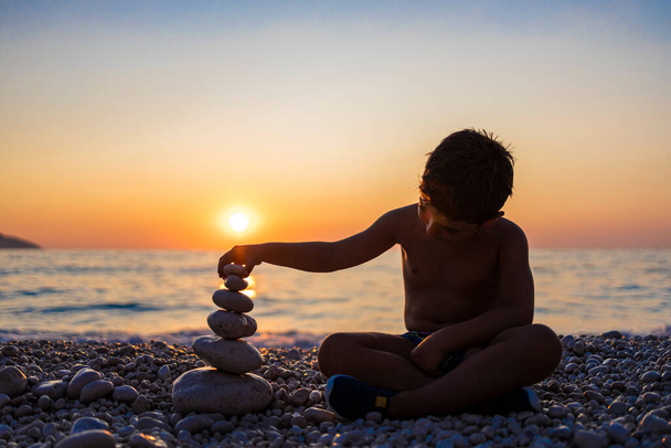 Kisgyerek játszik kövekkel a parton naplementekor - Fotó, kép
