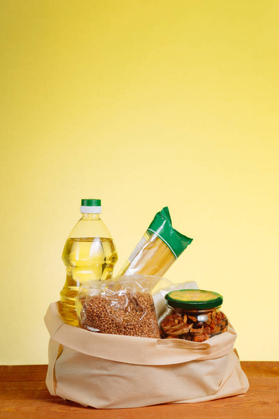異なる食品で紙袋上の木製のテーブル、黄色の背景。食料品店のコンセプト. - 写真・画像