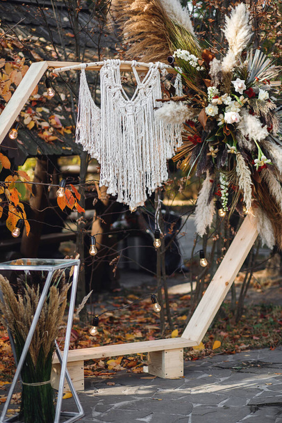 Svatební obřad s obloukem v rustikálním stylu s makramem. Svatební ceremoniál s dřevěným obloukem s čerstvými květy a trávou - Fotografie, Obrázek
