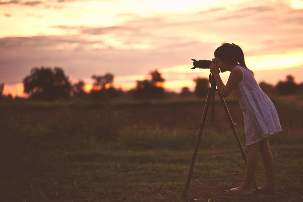 Asijské holčička fotograf pořízení fotografie silueta západ slunce obloha podle digitální fotoaparát na stativ stojící s šťastný. - Fotografie, Obrázek