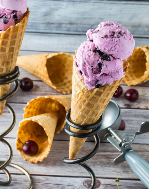 Una vista ravvicinata di un cono gelato alla ciliegia circondato da altri coni, ciliegie e uno scooper gelato
. - Foto, immagini