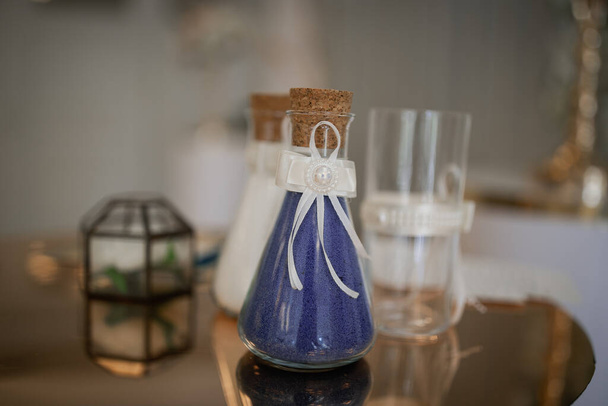 Arena decorativa en frascos de vidrio de color azul y blanco. Anillos de boda en una caja en el fondo en desenfoque
. - Foto, imagen