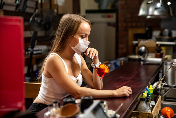 girls in medical masks drink cocktails.  girl in a medical mask is resting in a pub. girl in a medical mask in a pub - Foto, Imagen