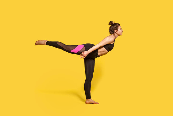 Warrior 3 pose. Slim woman with hair bun in tight sportswear practicing yoga, doing Virabhadrasana III exercise on one leg, stretching muscles and balancing. studio shot, sport workouts isolated - Фото, изображение