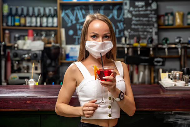 girls in medical masks drink cocktails.  girl in a medical mask is resting in a pub. girl in a medical mask in a pub - Photo, image