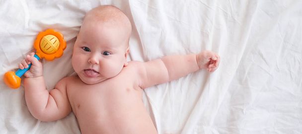 Banner. baby boy with red toy on white blanket. Newborn child relaxing in bed. Family morning at home. Copyspace - Foto, Bild