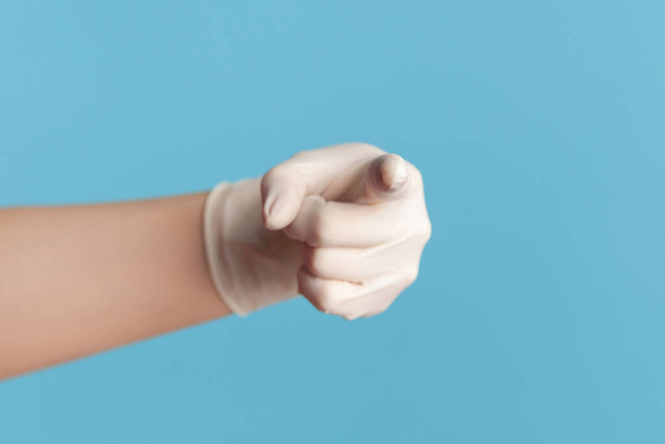 Profile side view closeup of human hand in white surgical gloves showing or pointing at camera. indoor, studio shot, isolated on blue background. - Foto, Imagem