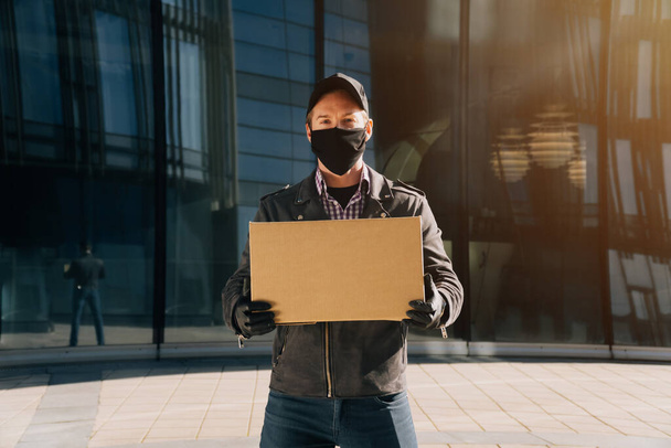 Home delivery male worker in medical mask and gloves holds a paper box with food - Photo, Image