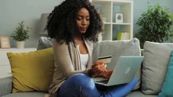 Pretty African American young woman online shopping with credit card using her laptop. Living room. - Video