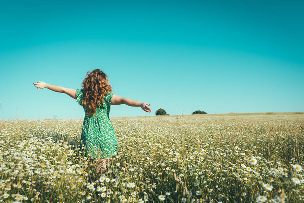 mujer en la espalda con los brazos abiertos en un campo de margaritas
 - Foto, Imagen